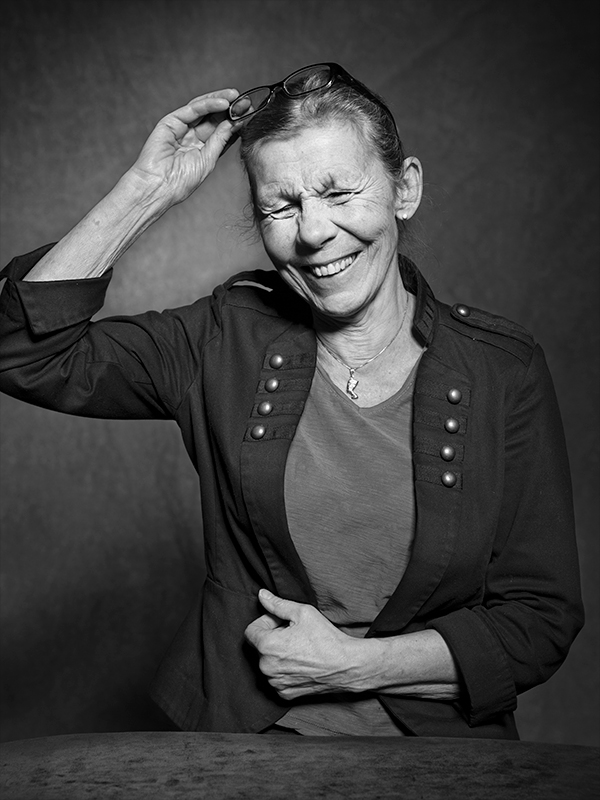 Svartvitt porträtt på en kvinna som ler stort och har handen på huvudet.