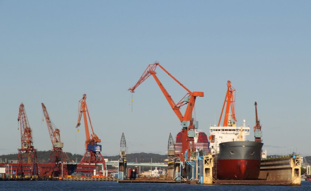 Orange kranar mot blå himmel, ett fartyg ligger i en docka.